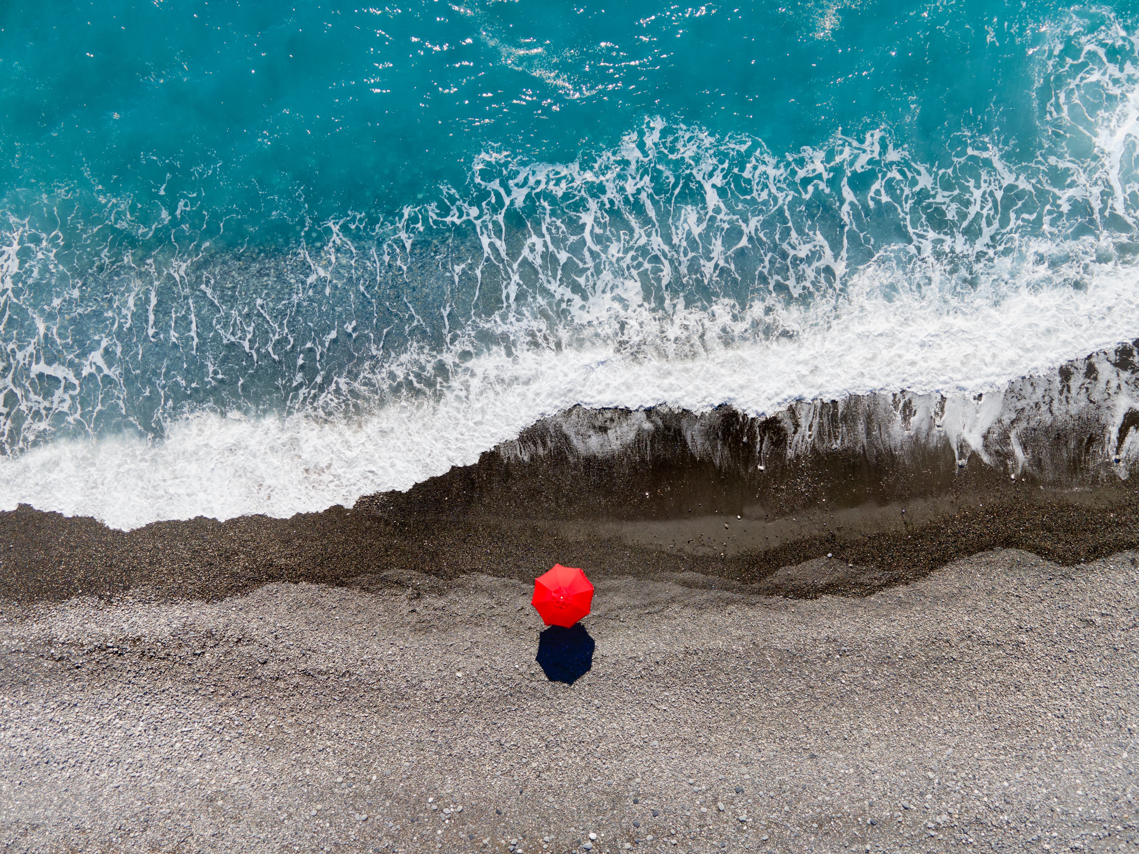 Spiaggia di ciottoli a picco sul mare turchese, ombrellone rosso visto dal drone — Isola d'Elba