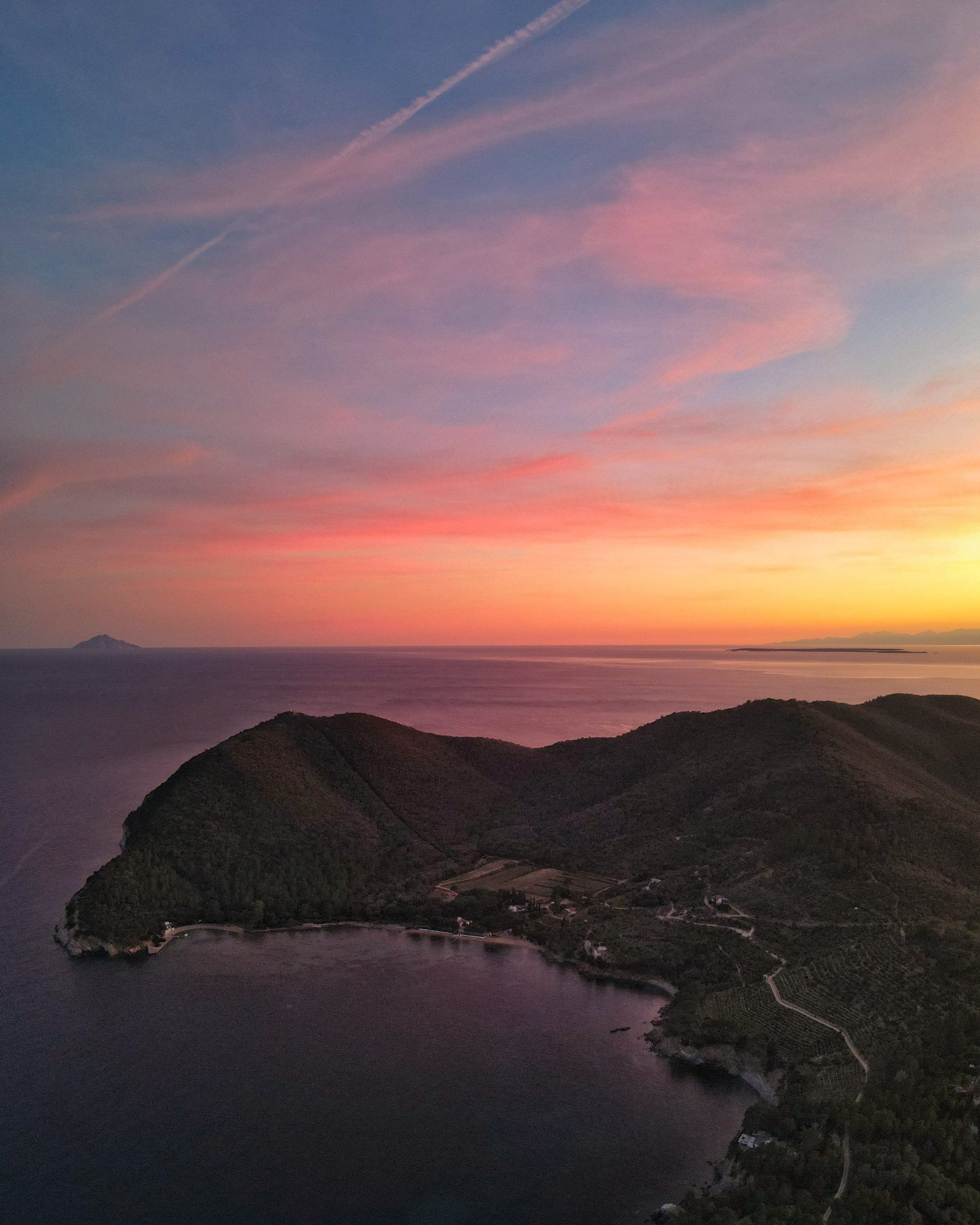 Promontorio dell'Elba al tramonto pastello, con Montecristo all'orizzonte