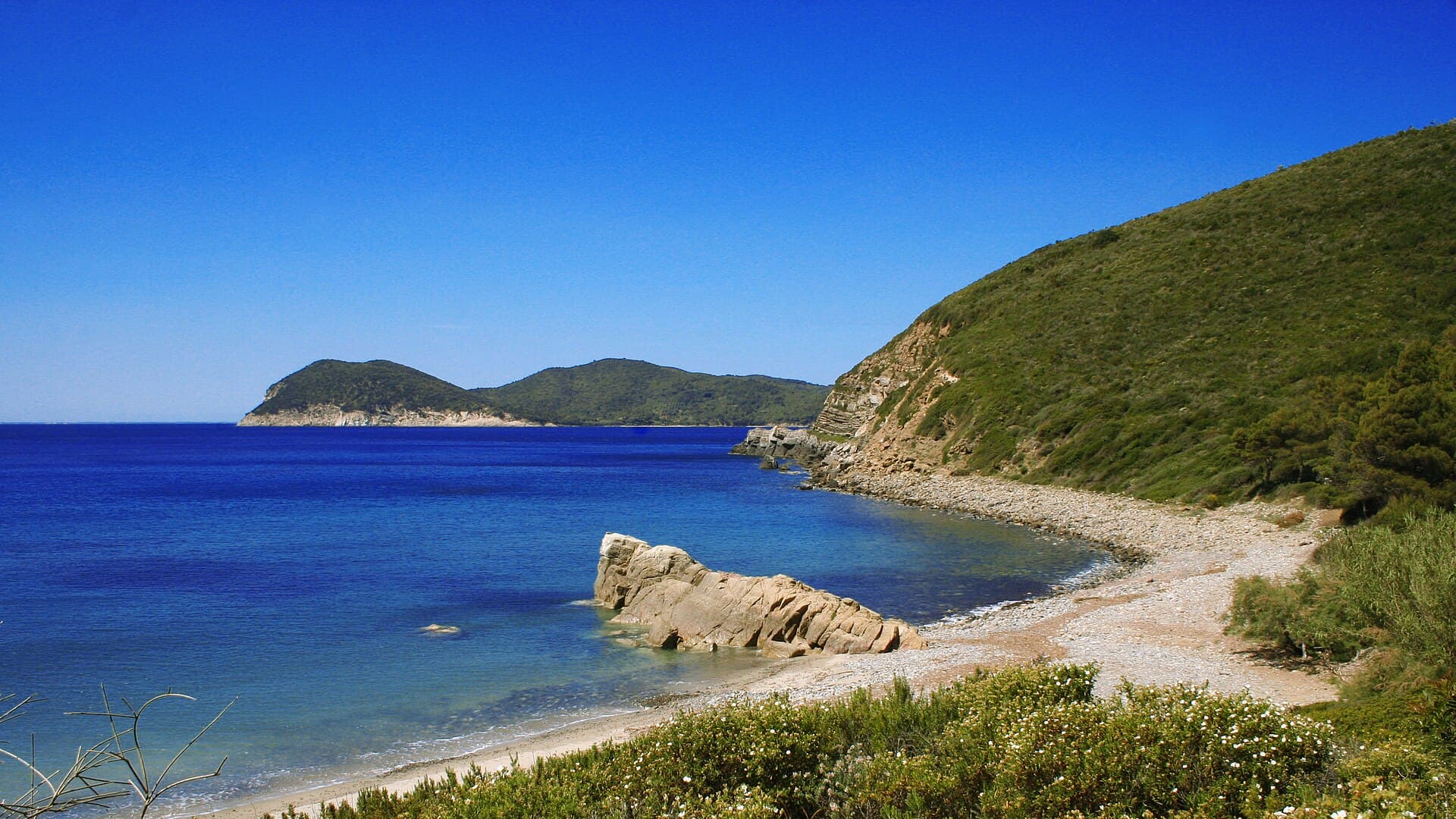 La cala di Fonza: sassi levigati, acqua blu profondo e la macchia mediterranea sul promontorio